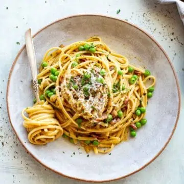 A plate of pasta carbonara with peas and a fork with pasta twisted around it.