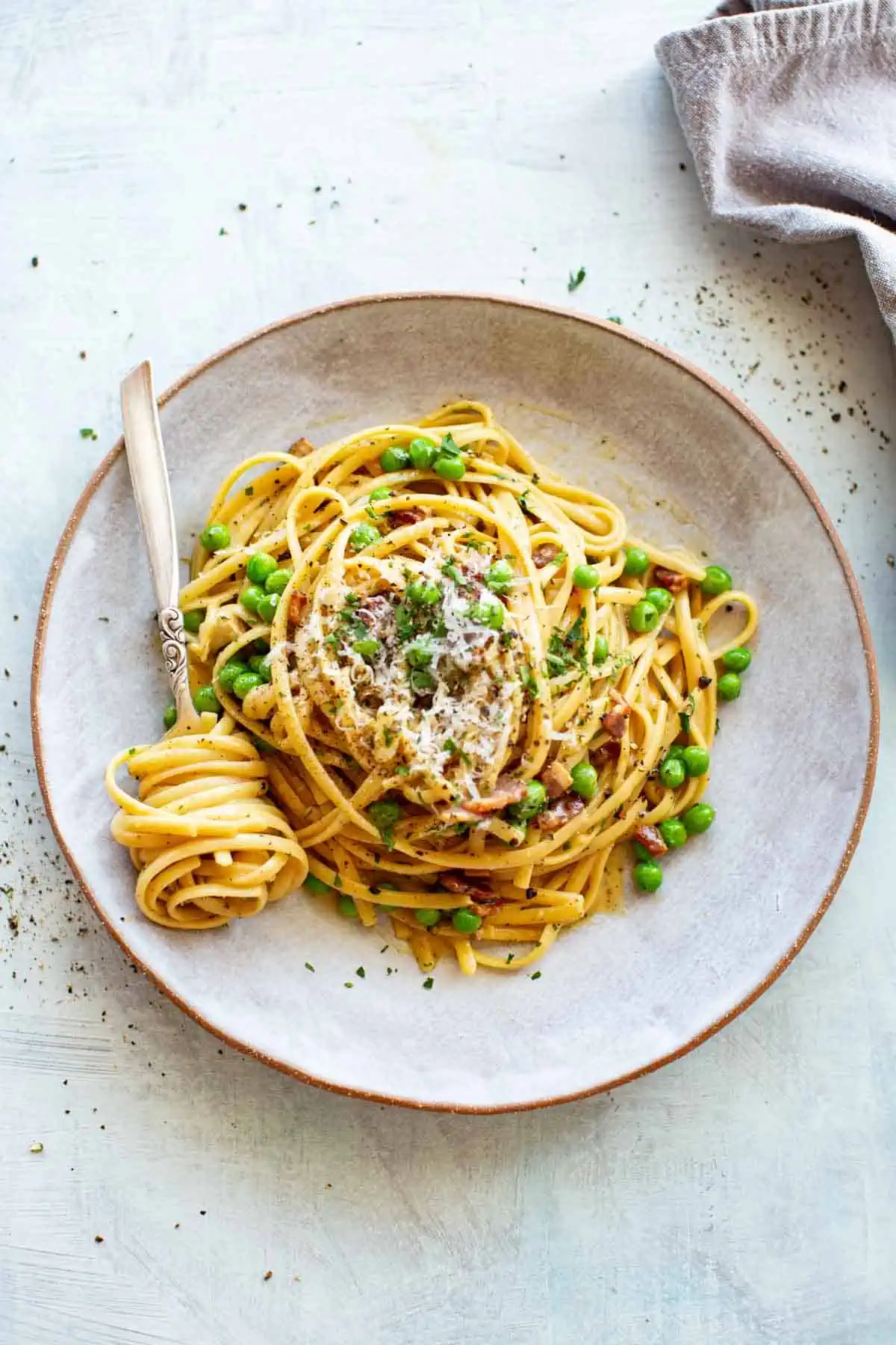 A plate of pasta carbonara with peas and a fork with pasta twisted around it.