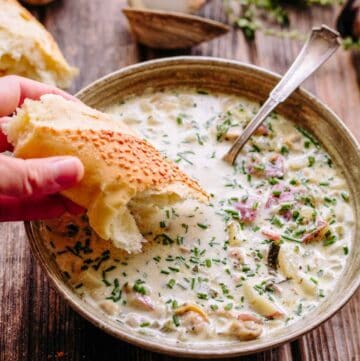 A bowl of New England clam chowder with a hand dipping bread.