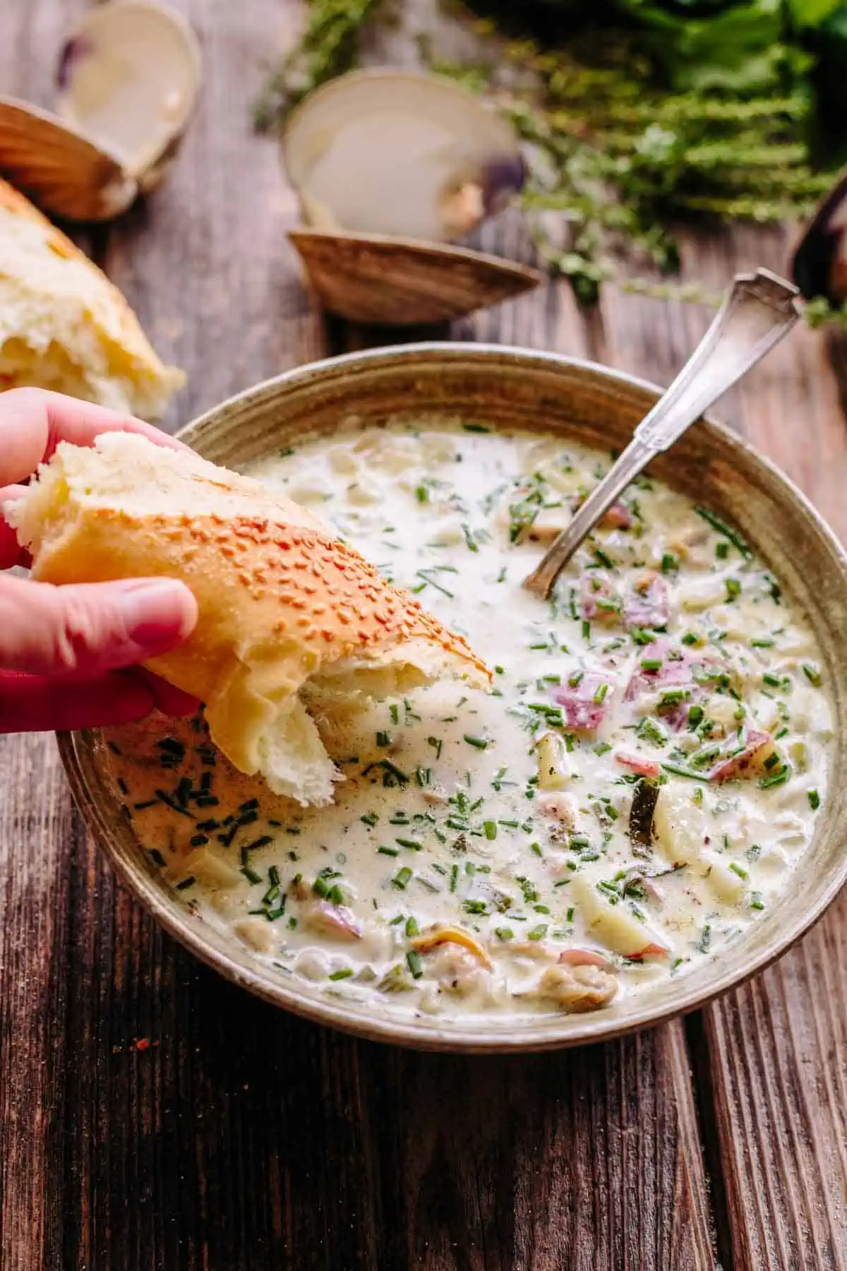 A bowl of New England clam chowder with a hand dipping bread.