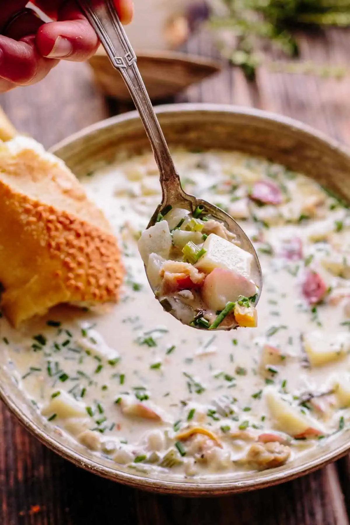A spoon full of clam chowder over a bowl.