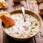 A bowl of New England clam chowder with a hunk of bread and a spoon.