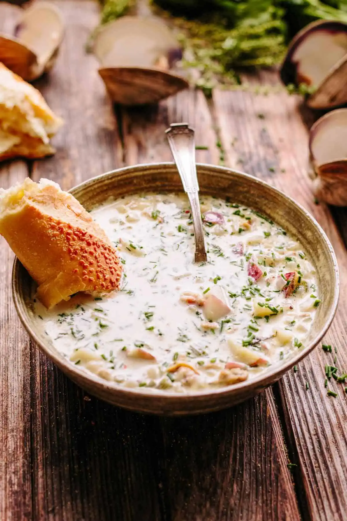 A bowl of New England clam chowder with a hunk of bread and a spoon.