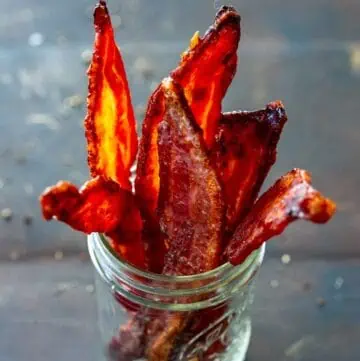 Side view of a mason jar filled with thick cut candied bacon.