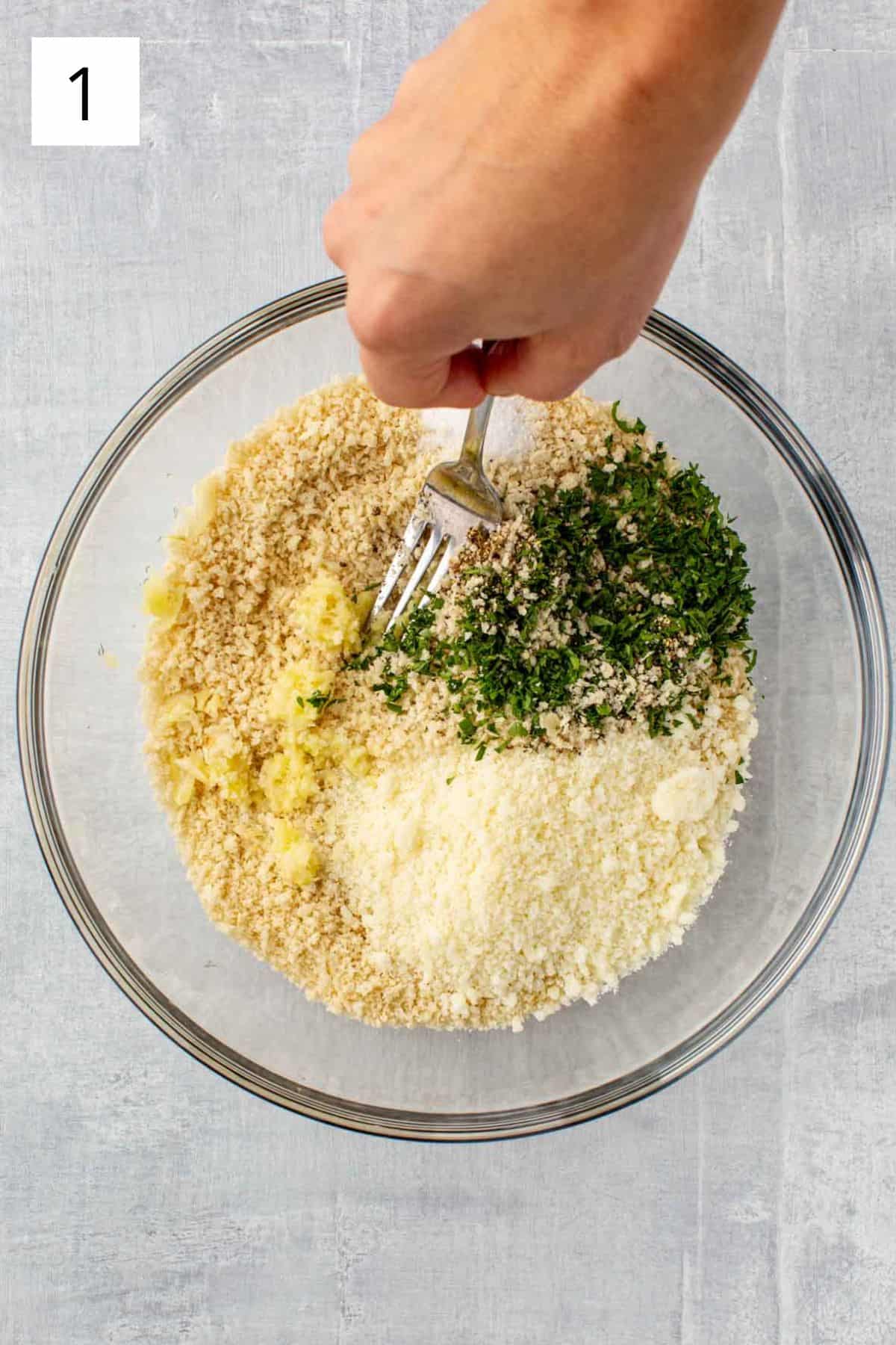 A fork mixing cheese and herbs into a bowl of breadcrumbs.