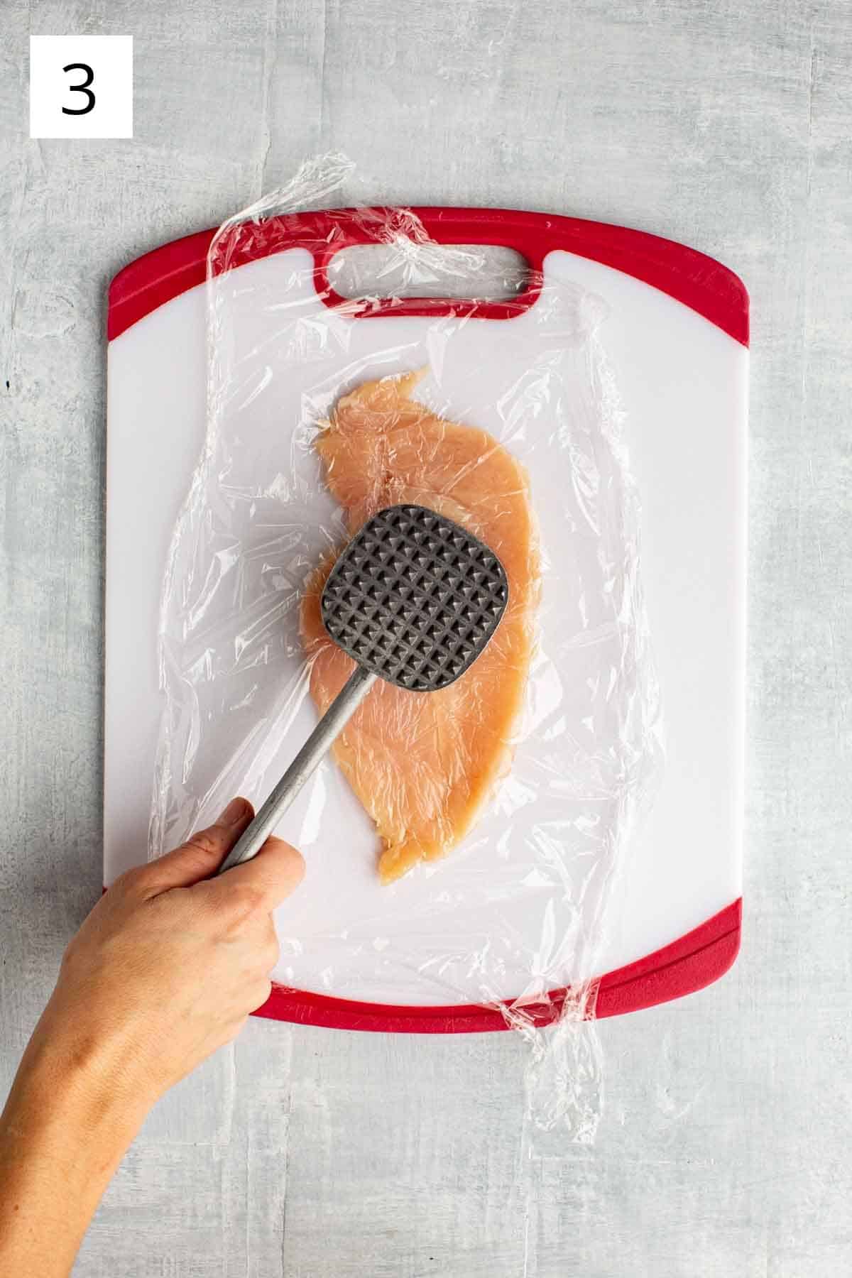 A chicken breast being pounded with a meat mallet.