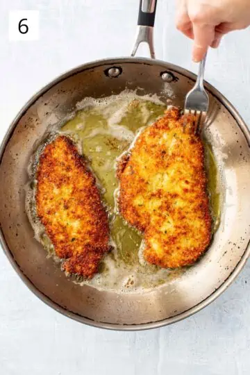 A fork poking a breaded chicken breast frying in a pan.