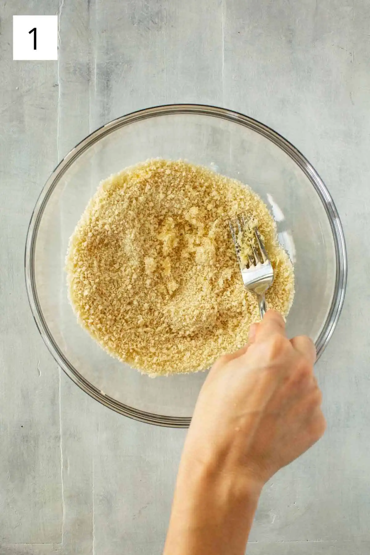 A fork mixing grated garlic into a glass bowl of panko breadcrumbs.