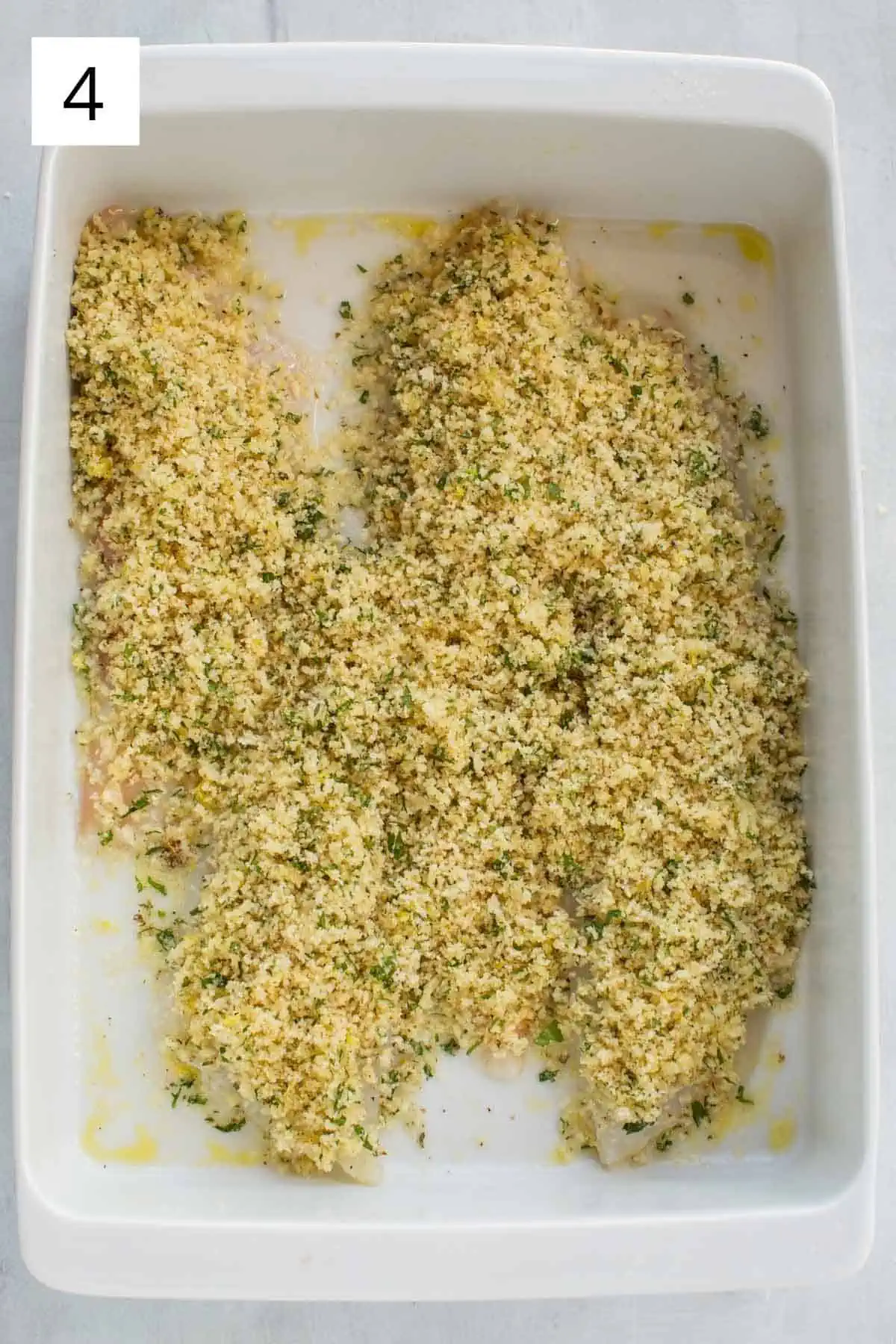 Flounder fillets in a baking dish topped with seasoned breadcrumbs before being baked.