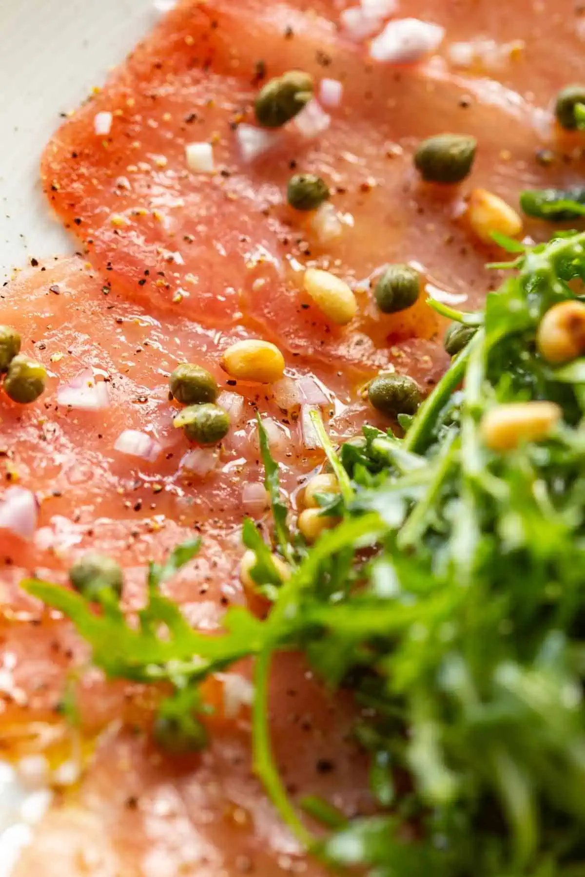 Close up of thinly sliced raw tuna with pine nuts and capers.
