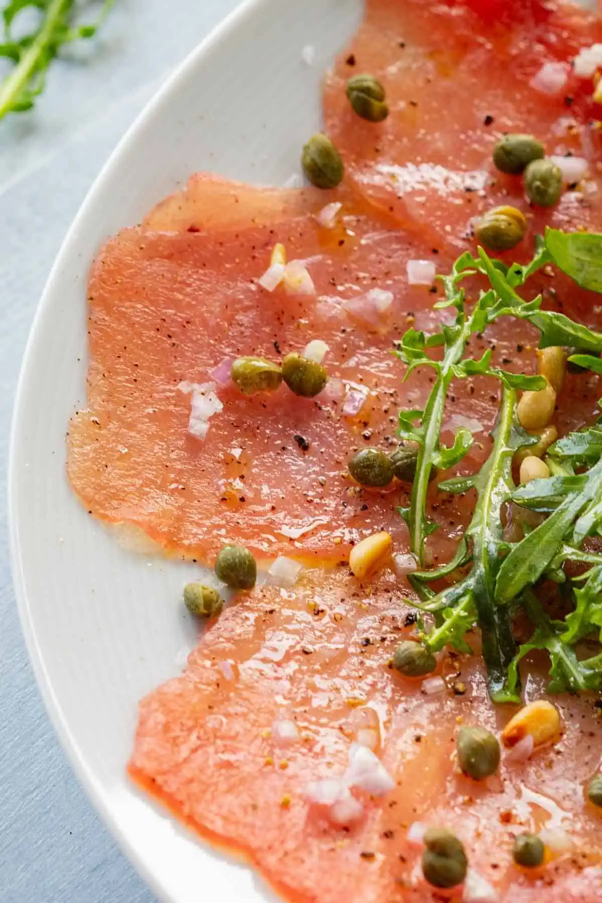 Top view close up of a plate of classic tuna carpaccio with arugula, capers and pine nuts.