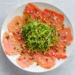 Top view of a plate of tuna carpaccio with arugula in the center.