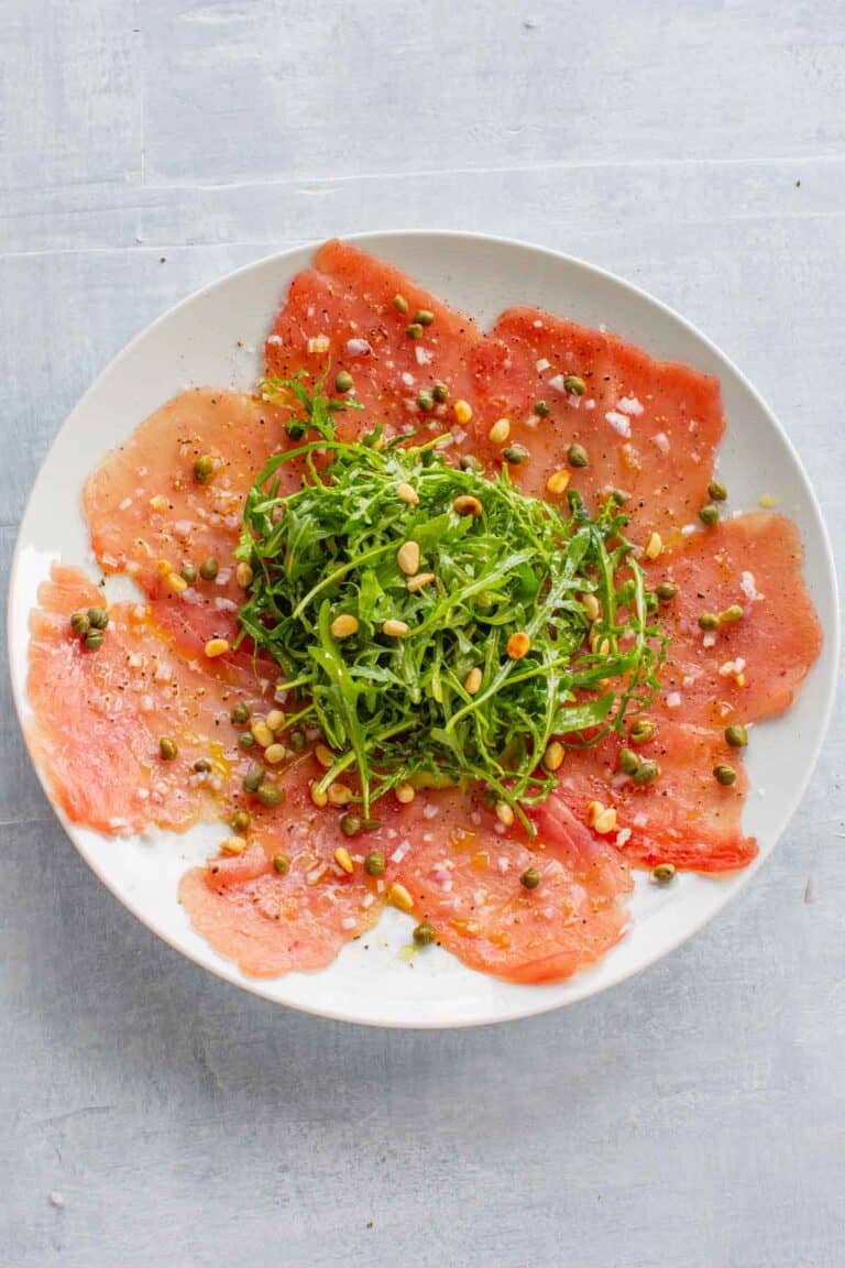 Top view of a plate of tuna carpaccio with arugula in the center.