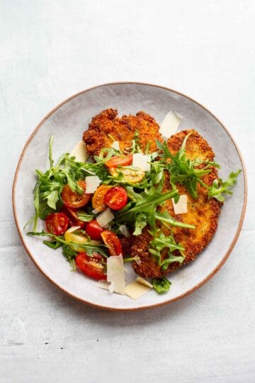 Overhead shot of a plate of crispy chicken Milanese with tomato arugula salad.