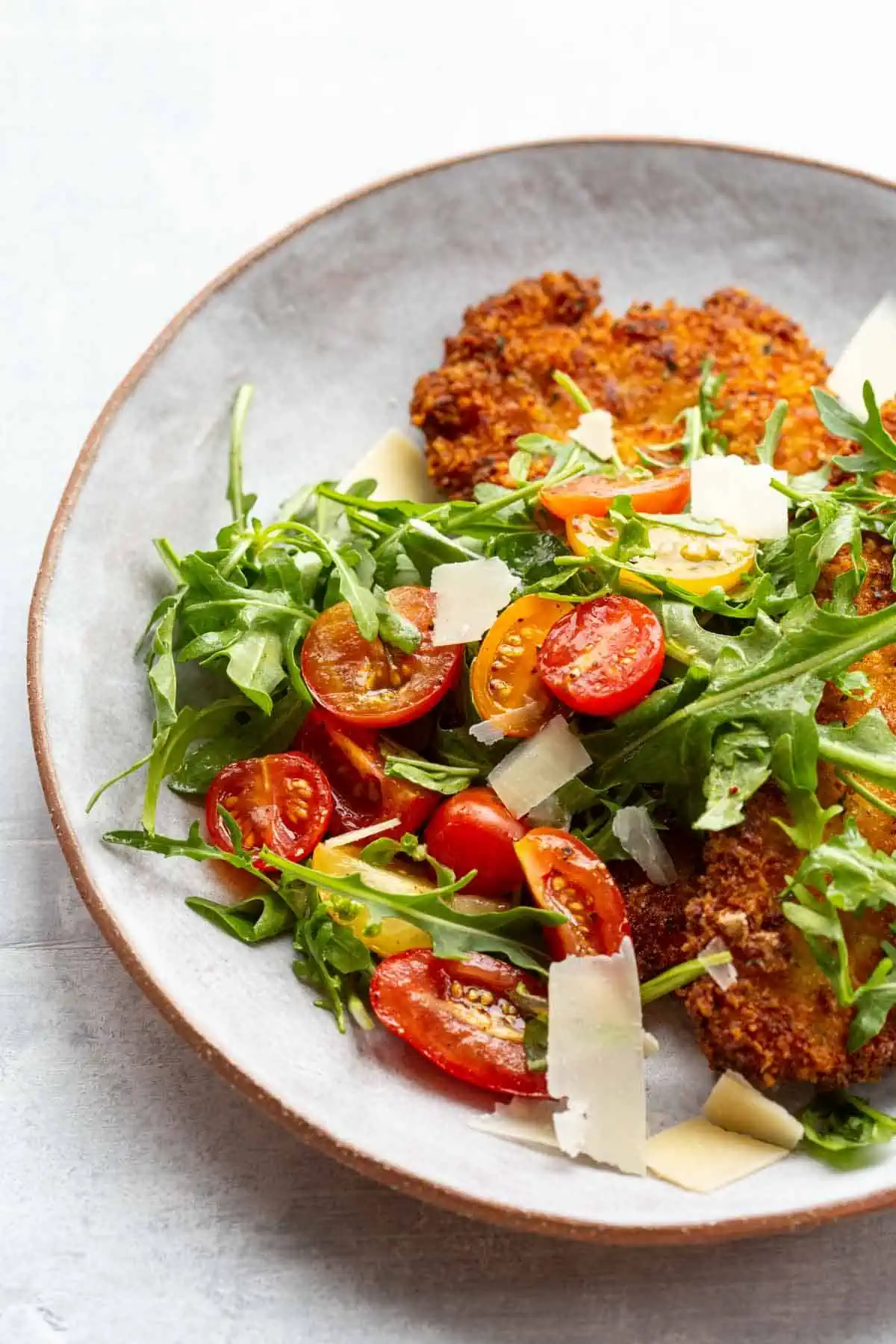 Close up of a plate of chicken Milanese with tomato arugula salad.