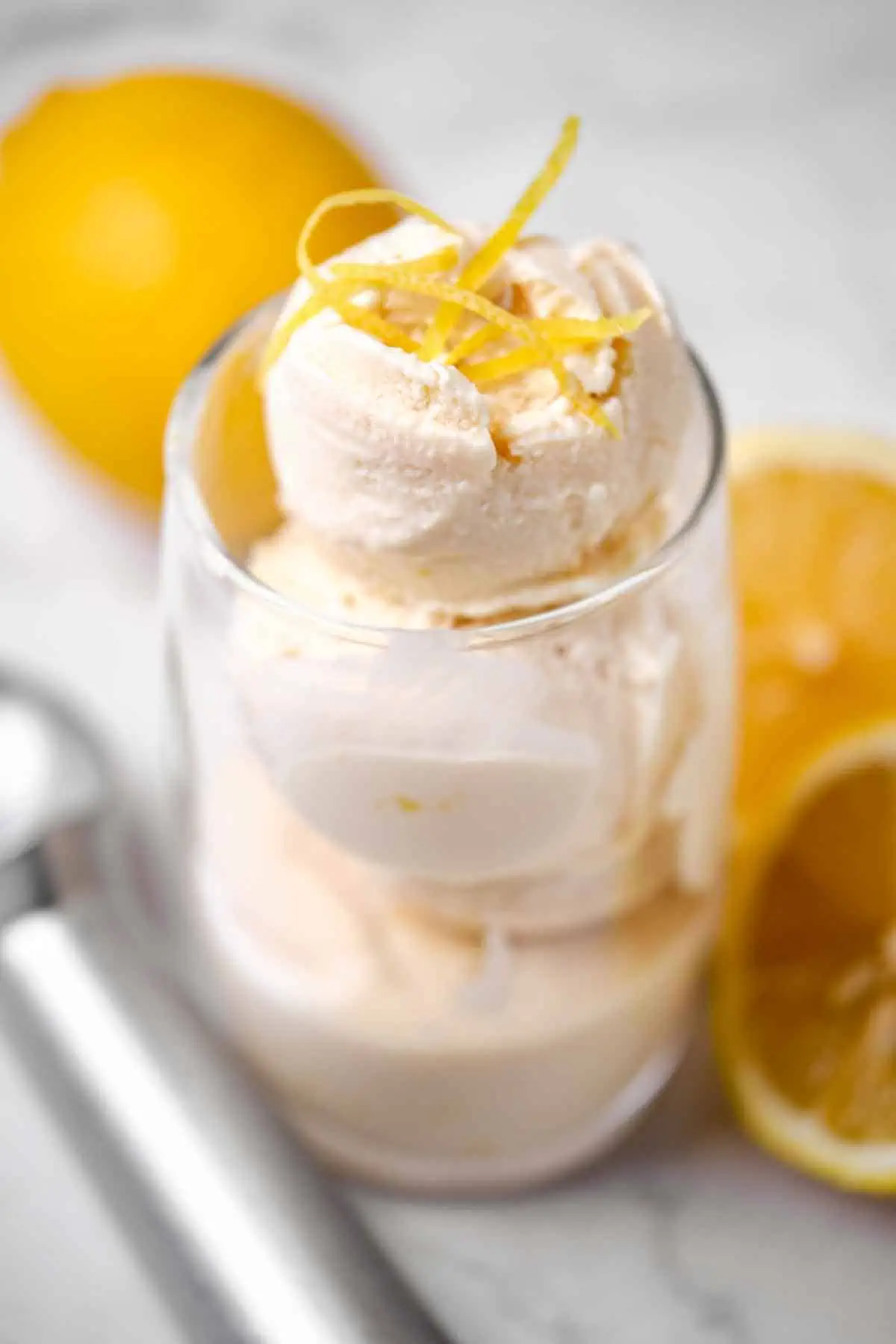 A clear glass filled with 3 scoops of lemon ice cream with fresh lemons and zest to garnish.