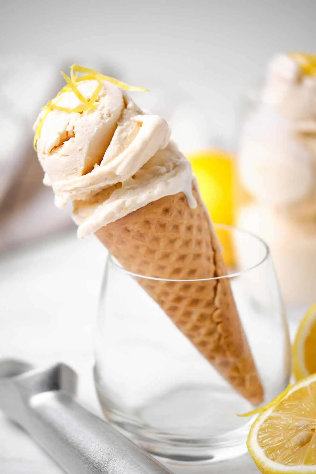 A clear glass holding an ice cream cone of lemon ice cream.