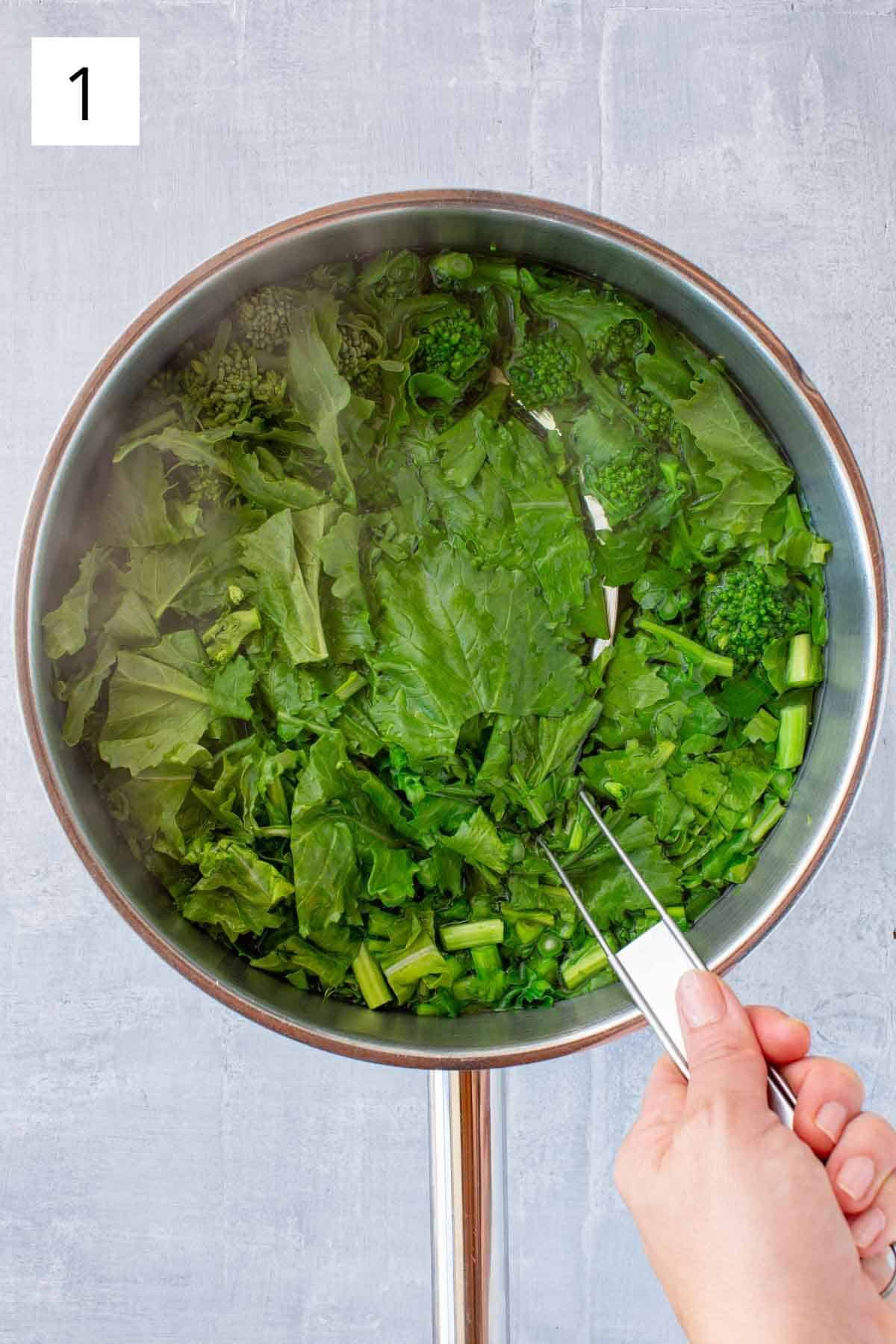 A strainer scooping broccoli rabe out of boiling water.