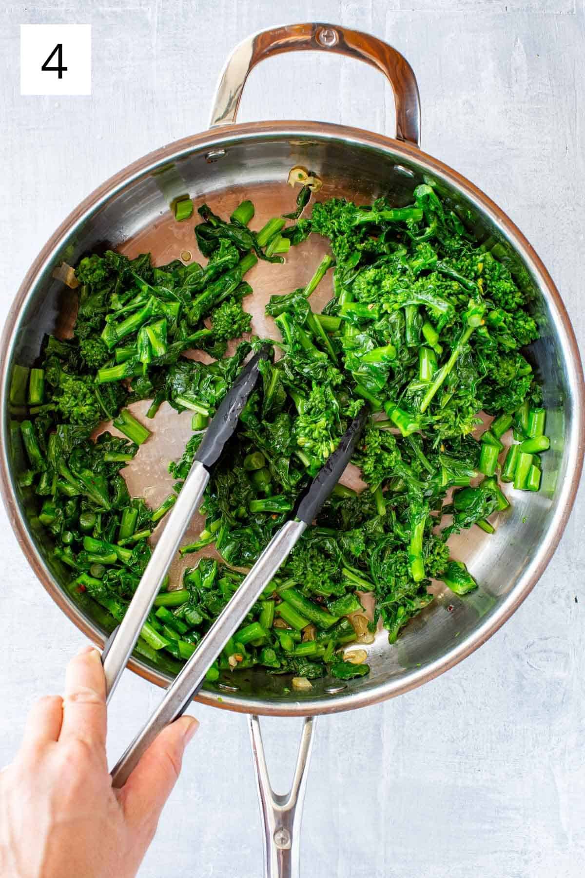 A pan of broccoli rabe being sautéed with a pair of tongs.