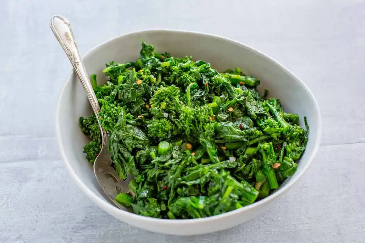 A bowl of sautéed broccoli rabe with a serving spoon.