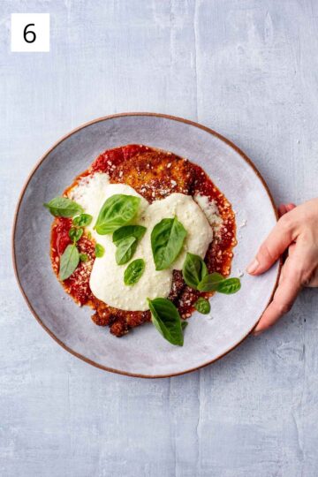 Plate of homemade chicken parmesan with melted mozzarella cheese, sauce, and fresh basil.