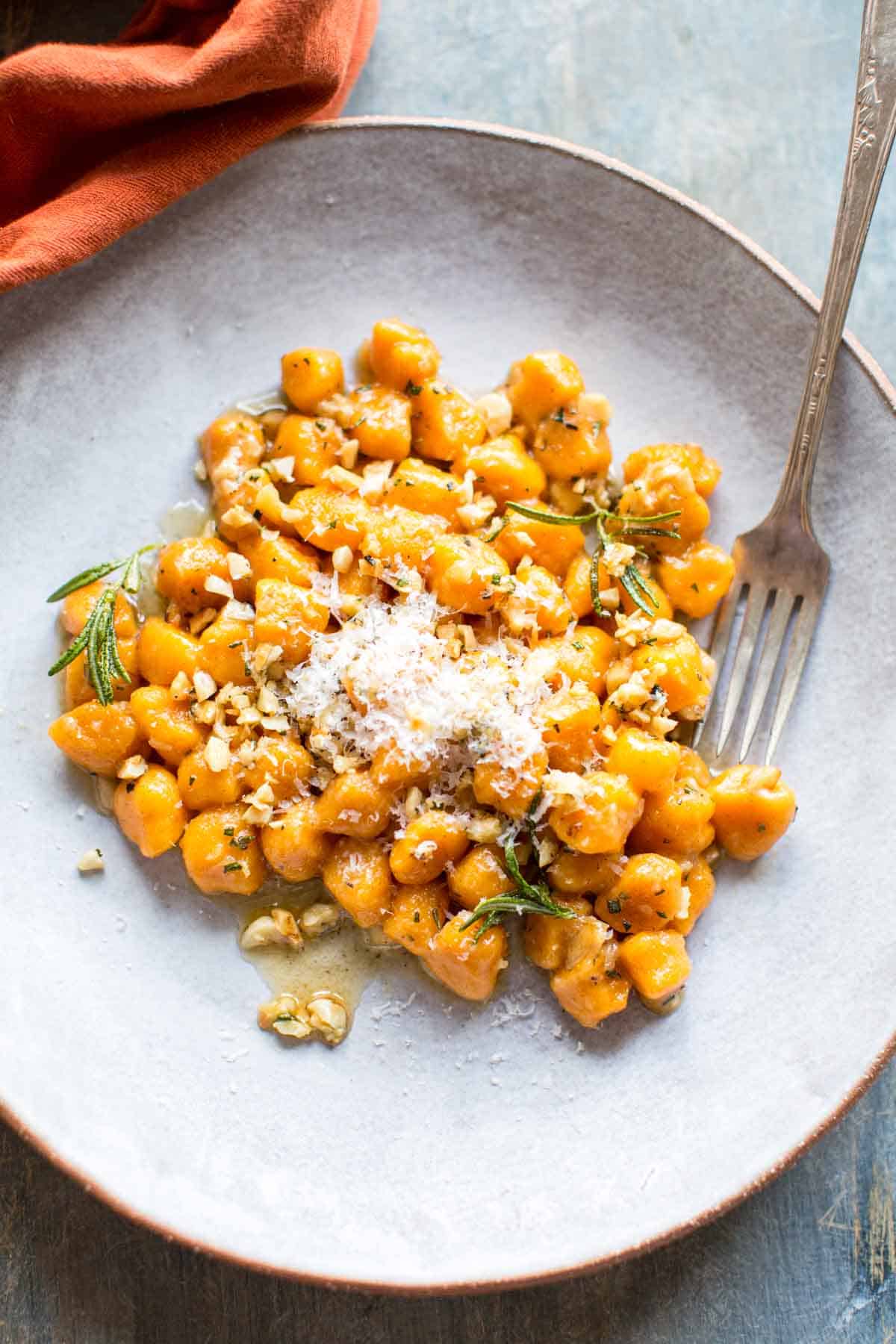 Close up of a finished sweet potato gnocchi recipe on a white plate, topped with chopped roasted nuts.