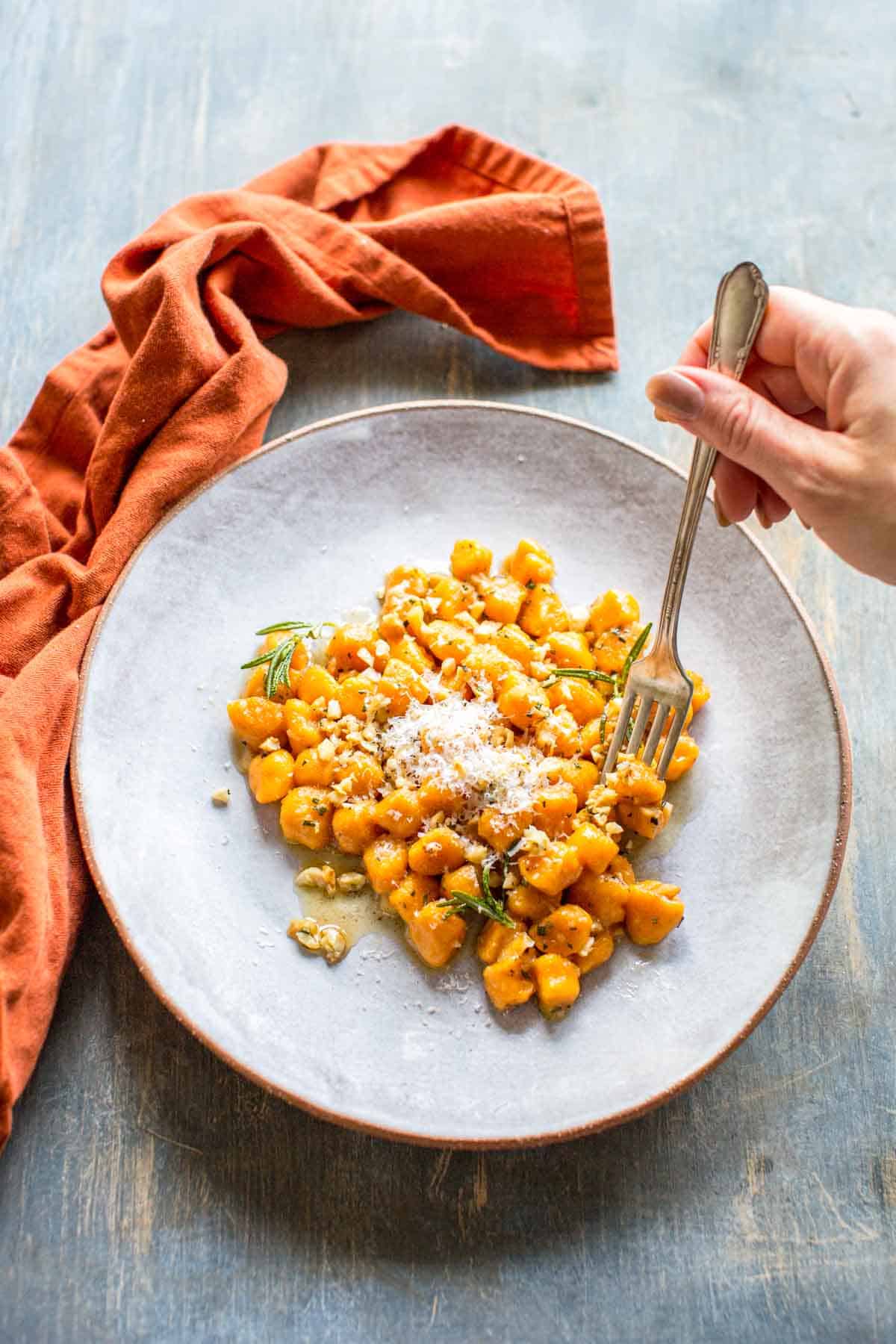 Aerial view of a fork piercing sweet potato gnocchi on a white plate. 