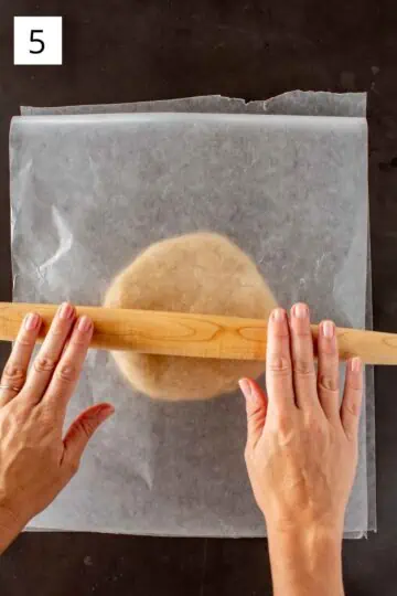 Using a wooden rolling pin to roll out dough between sheets of wax paper. 