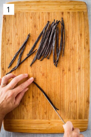 Cutting down the center of vanilla beans on a wood surface.