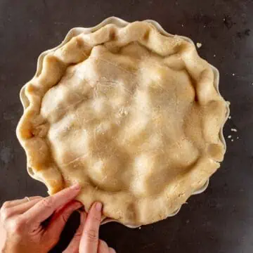 Two fingers crimping the dough on a pie.