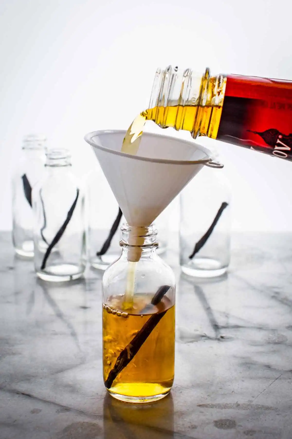 Pouring homemade extract through a funnel into a smaller glass bottle.