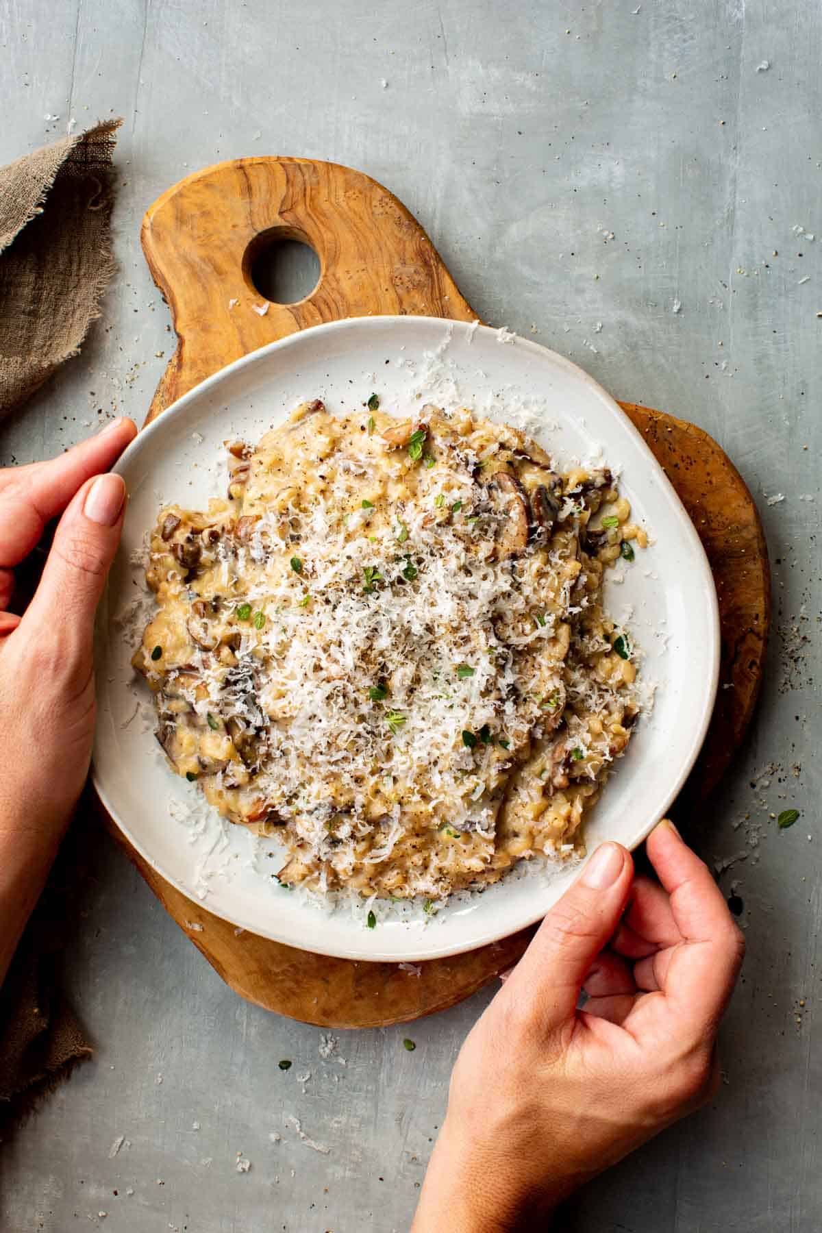 Hands holding a white plate filled with creamy wild mushroom risotto.