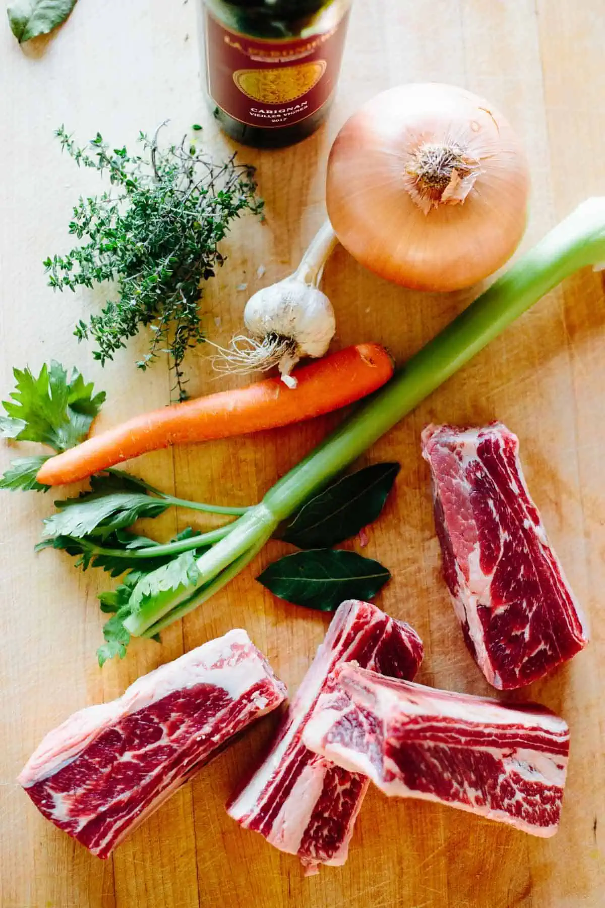 Fresh ingredients for short rib recipe laid out on a wood surface.