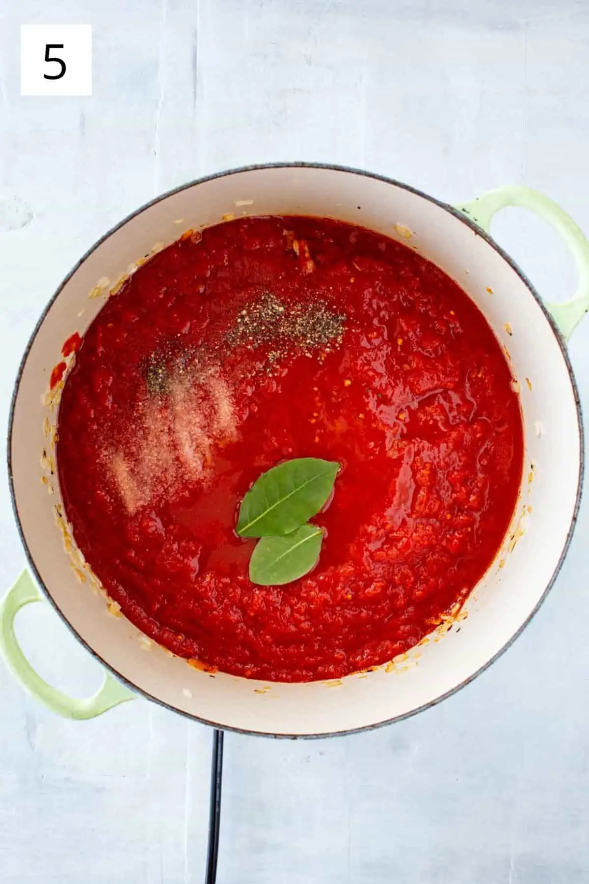 A Dutch oven with tomato sauce, bay leaves, salt and pepper.