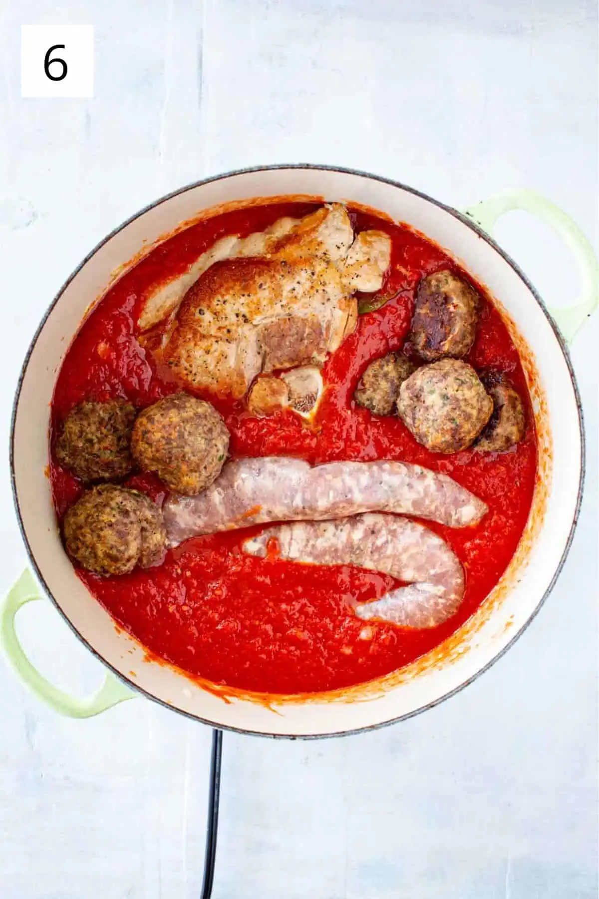 Italian sausage, meatballs and pork loin being added to a pot of red gravy.