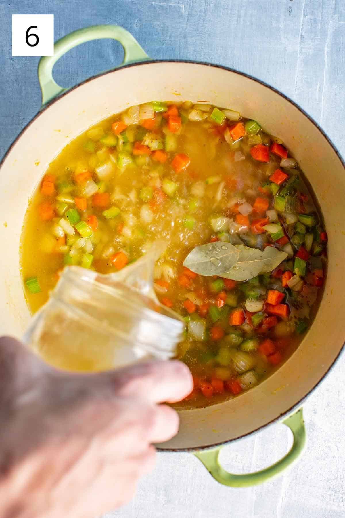 Adding broth to a pot of vegetables.