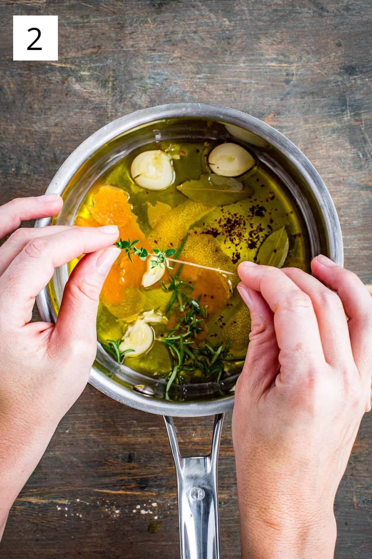 Hands picking thyme leaves from the stem over a pot of ingredients.