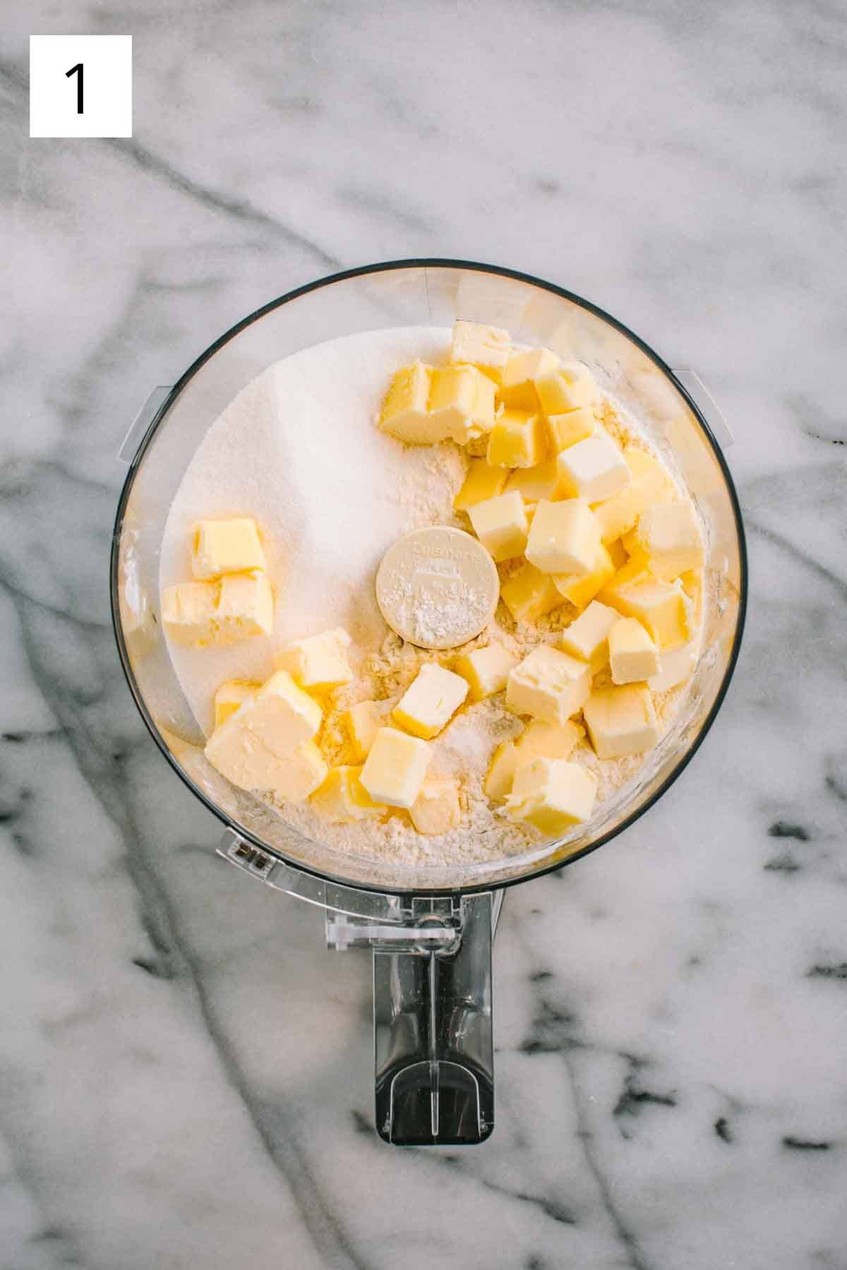 A food processor with flour, sugar and cubes of butter.