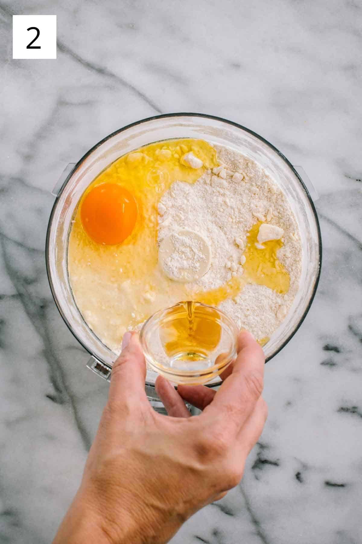 Pouring vanilla into a food processor with flour and an egg.