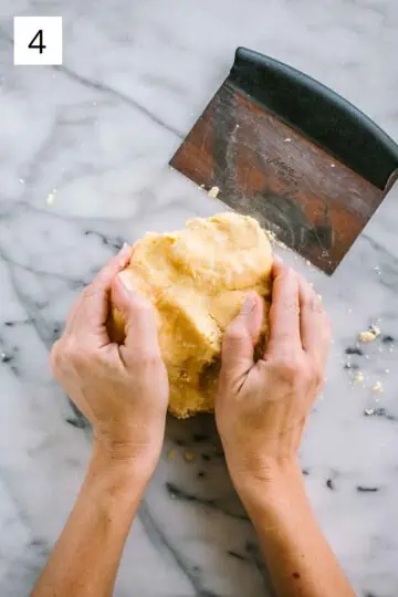 Hands kneading a ball of pastry dough with a bench scraper.