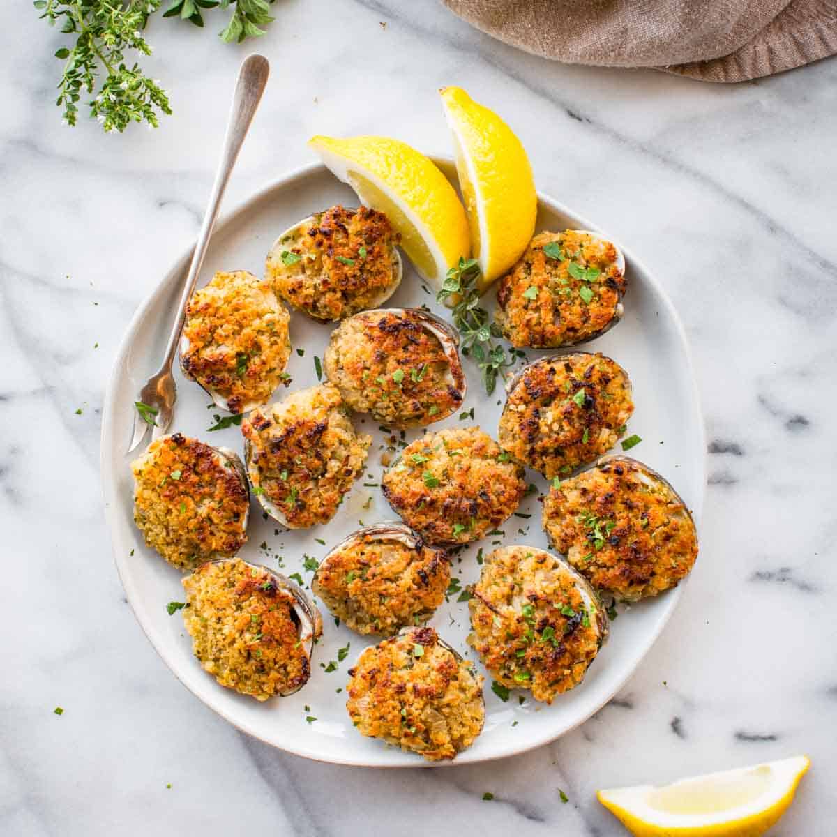 A plate of baked stuffed clams with lemons and a cocktail fork.