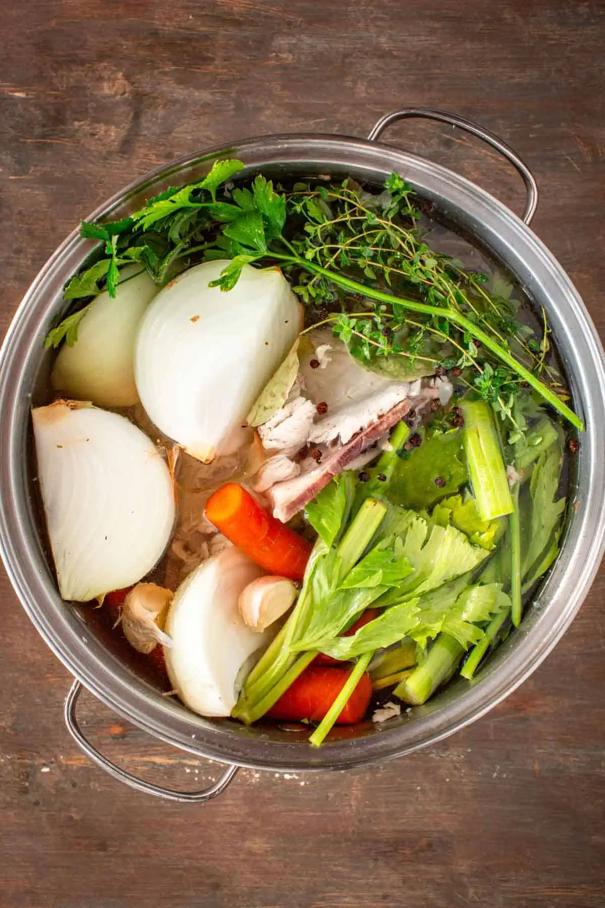 A pot filled with a turkey carcass, vegetables, herbs and water.