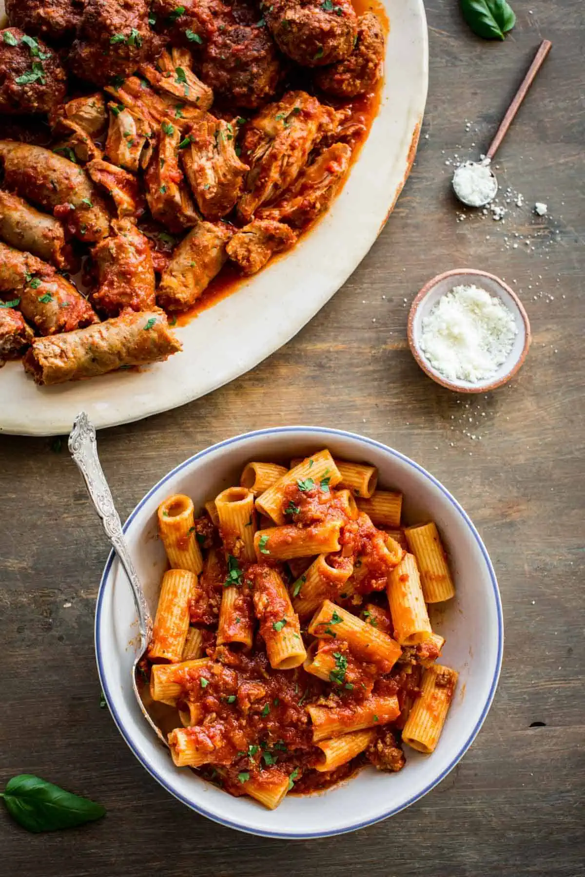 A bowl of rigatoni and red sauce a platter of braised meat.