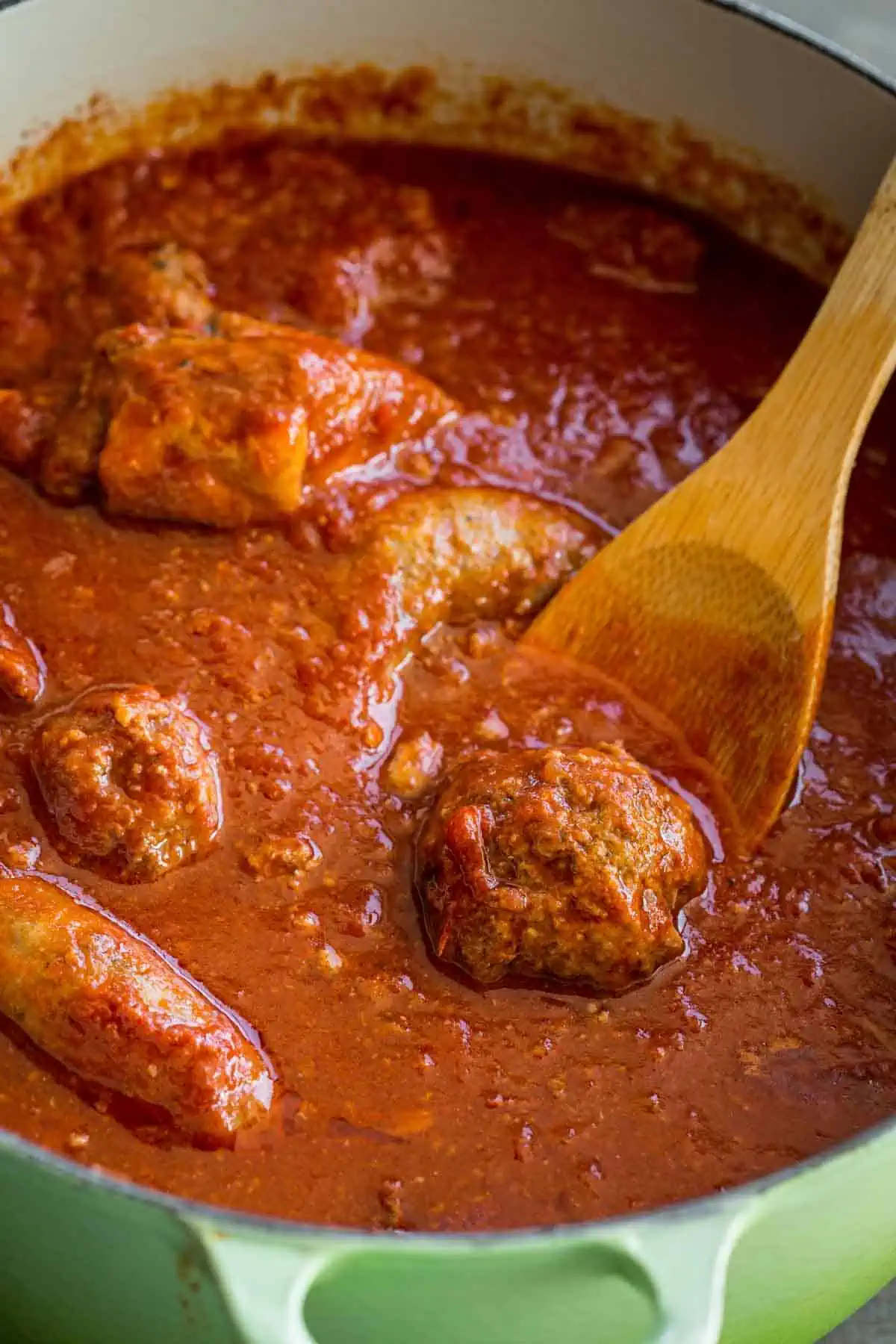 A wooden spoon lifting a meatball out of a pot of Italian red gravy.