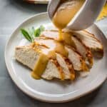 Turkey gravy being poured over sliced turkey breast.