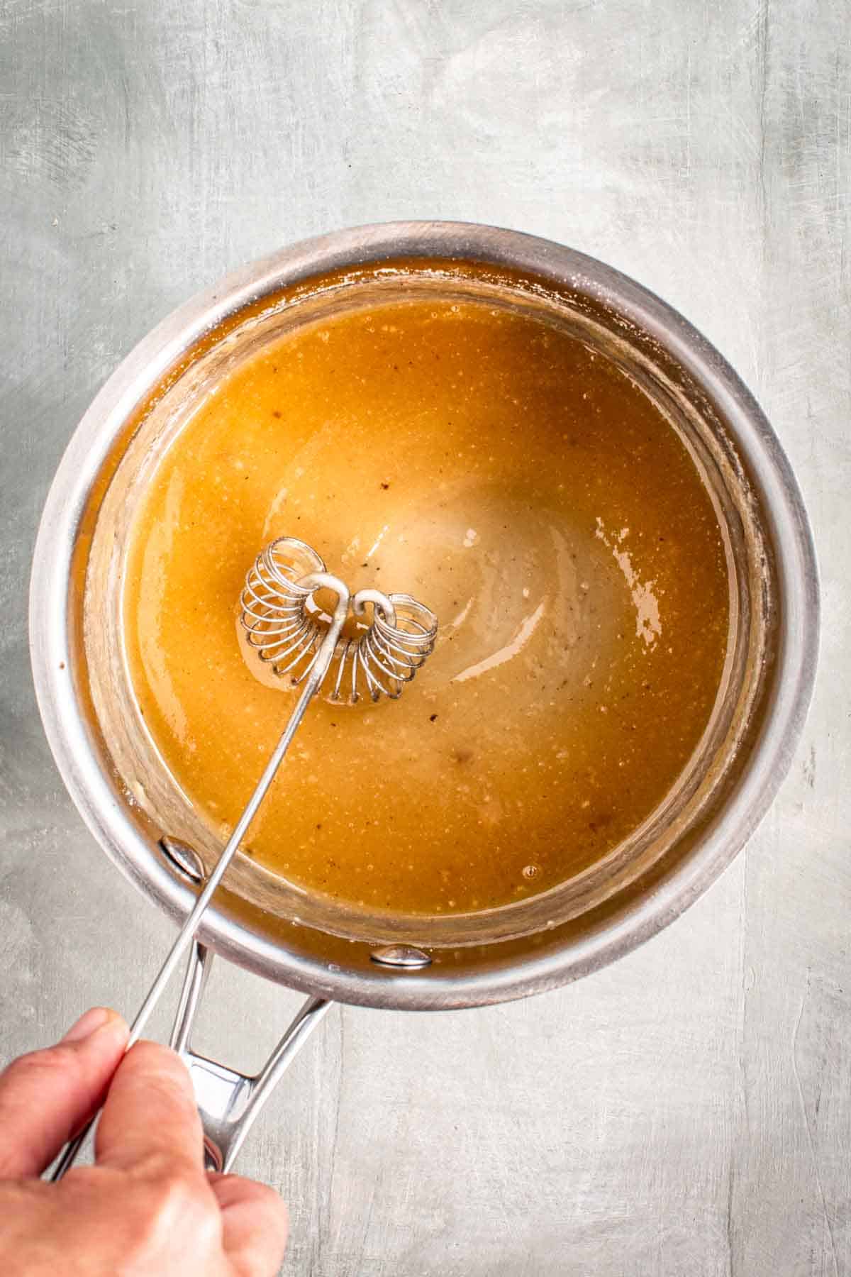 A hand whisking turkey gravy in a saucepan.