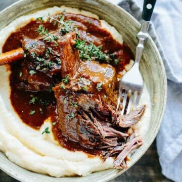 A bowl of slow cooked short ribs falling apart with a fork.