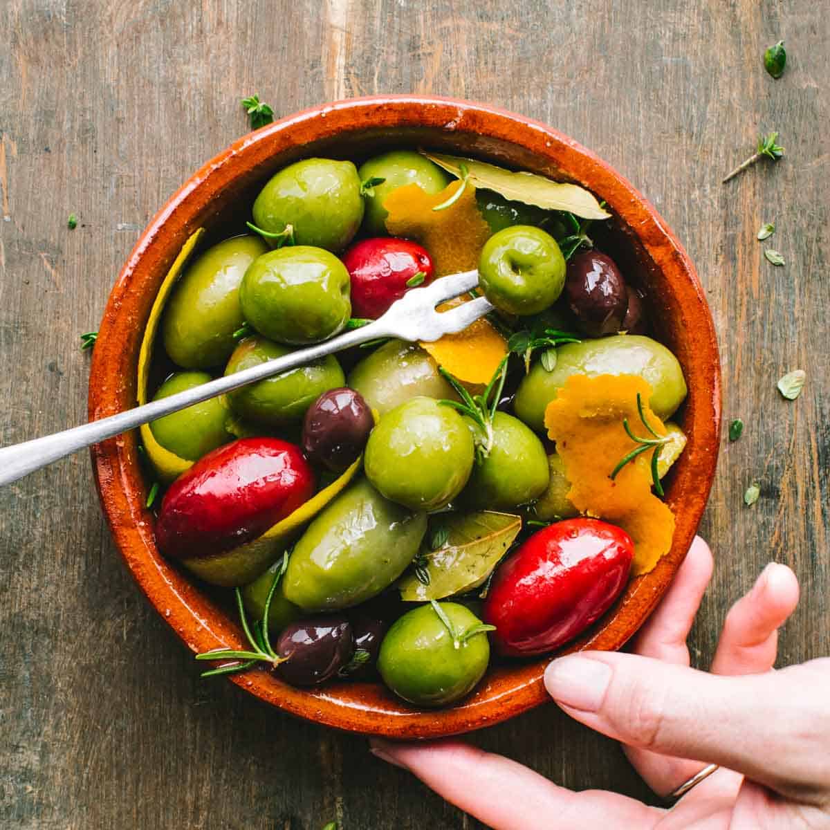 A bowl of citrus marinated olives with a cocktail fork.