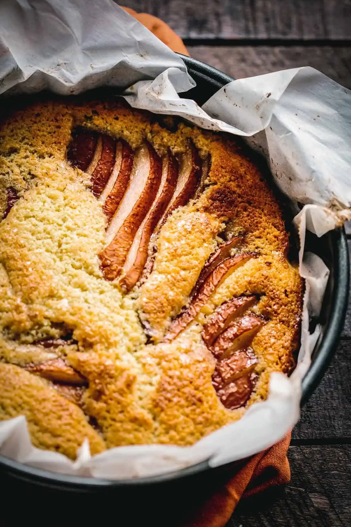 A baked pear ricotta cake in a parchment lined round cake pan.
