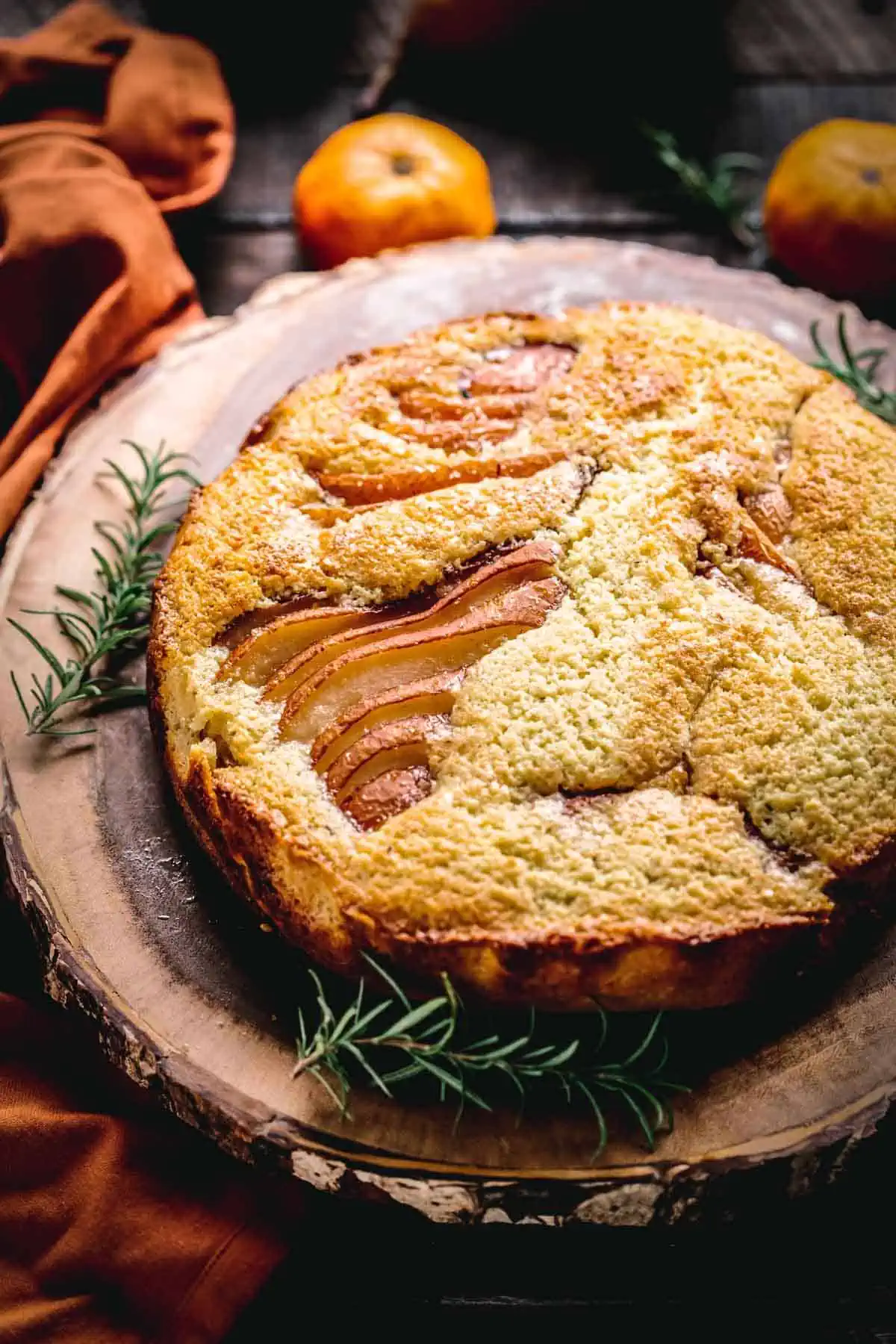 Italian ricotta cake with pears and sprigs of rosemary on a wood slab.